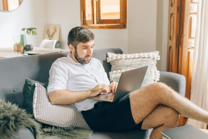 A man sitting on a sofa works from home on his laptop.