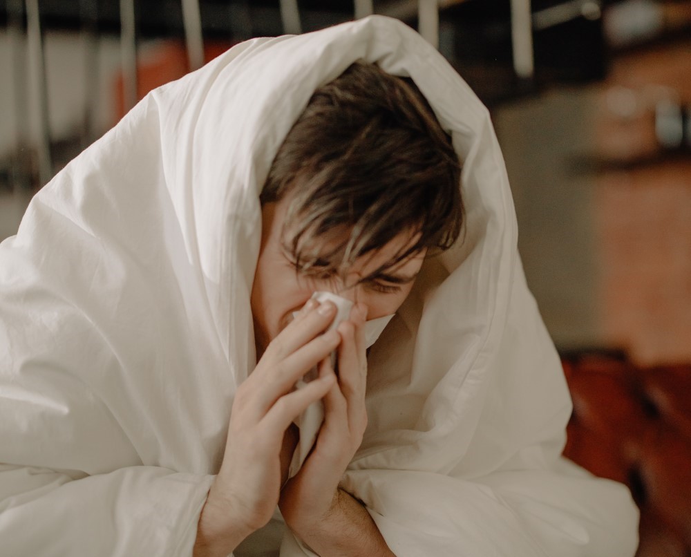 a sick employee sits at home with a duvet and blows his nose