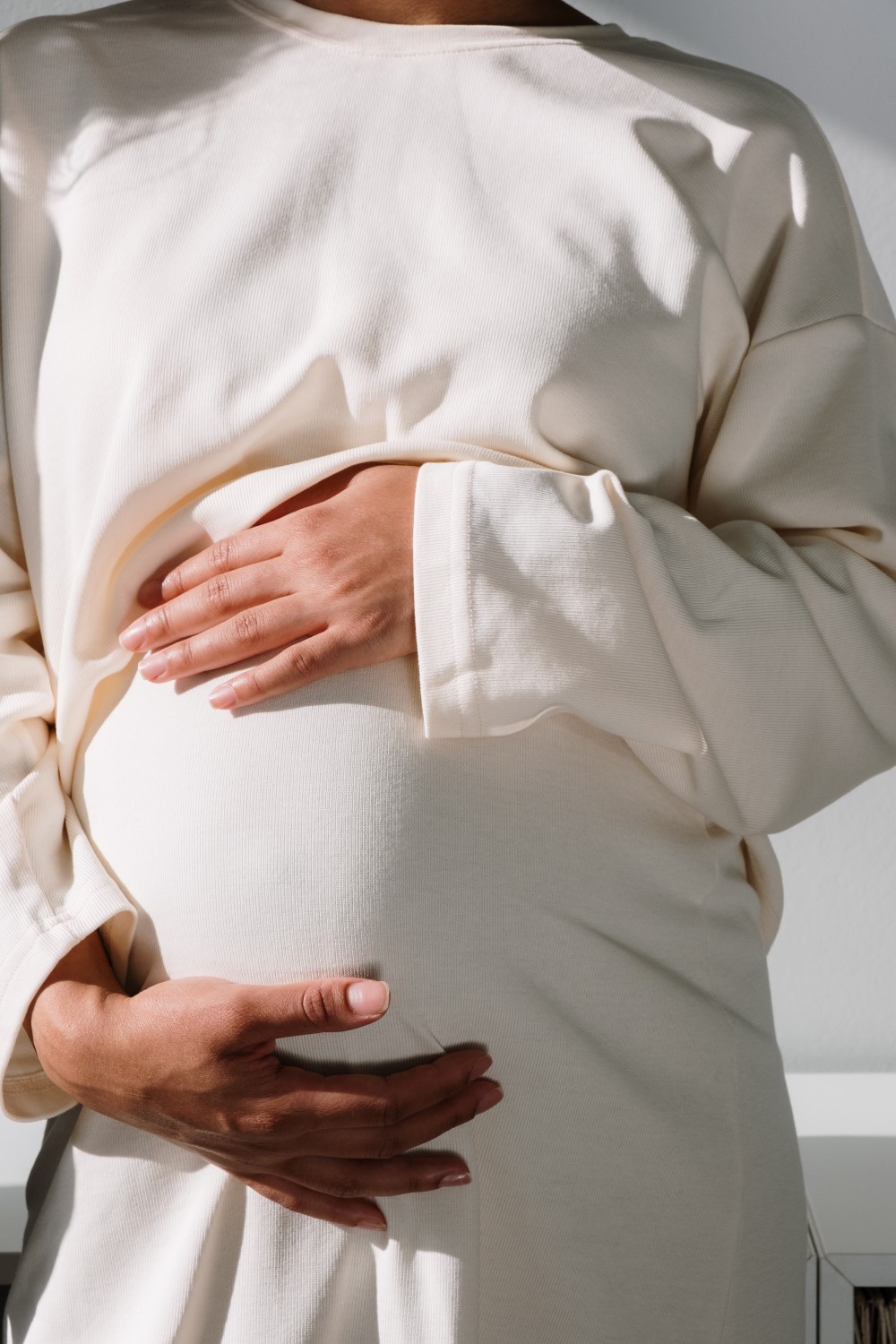 a pregnant women holds her tummy wearing a white dress